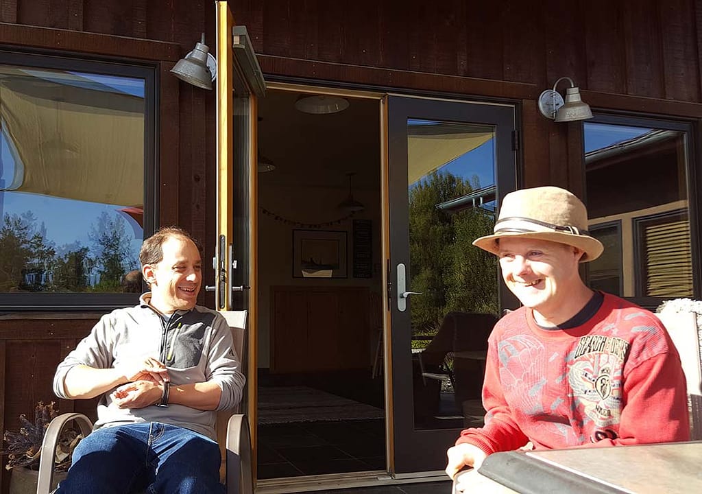 Two Camphill California residents hang out on a sunny porch laughing
