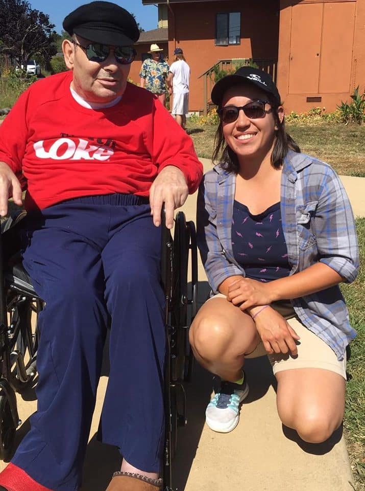a woman poses with a man sitting in a wheel chair outdoors