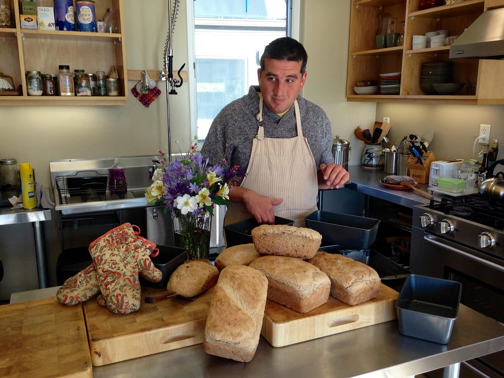 a man stands in a kitchen with six loaves of freshly baked bread